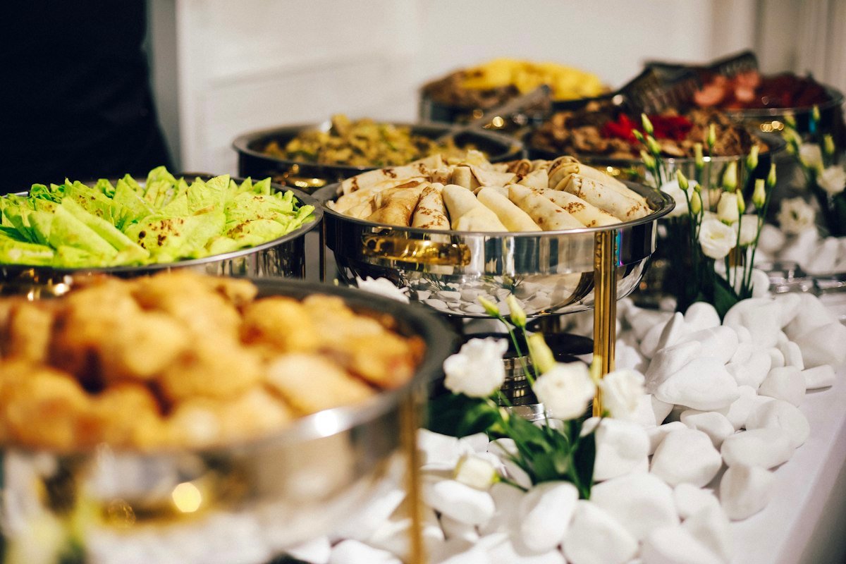 Mesa de buffet elegante con platillos variados servidos en chafers de acero inoxidable para evento de catering